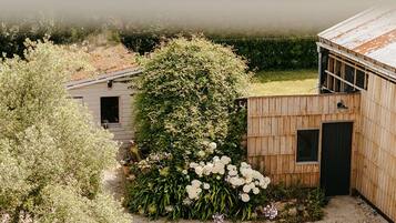 Uma cabana rústica com um caminho de acesso de brita, rodeada por vegetação densa e vista para um corpo d'água.