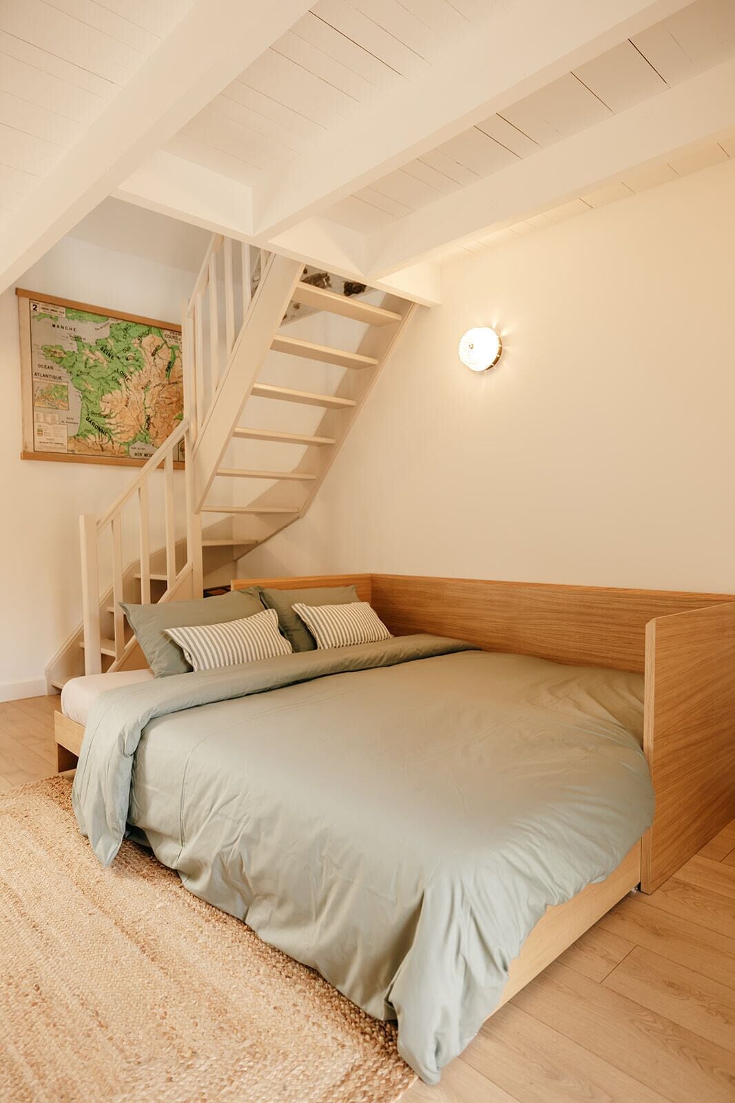 Une chambre à coucher avec un lit, une tête de lit en bois, un escalier et un luminaire fixé au mur.
