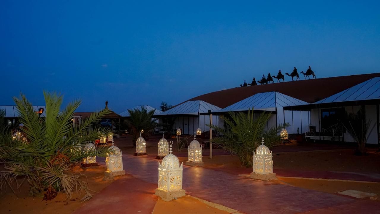A pathway lined with illuminated lanterns leading to a building with a red roof.