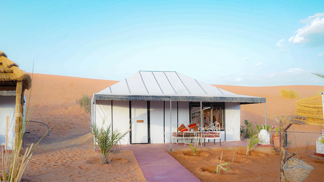A desert-style building with a flat roof, a covered outdoor seating area, and a paved entrance path.