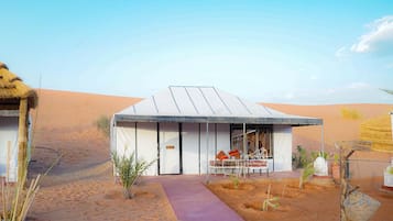 A desert-style building with a flat roof, a covered outdoor seating area, and a paved entrance path.