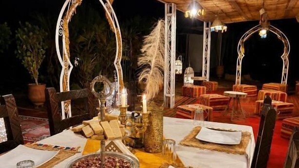 An outdoor dining area with tables set for a meal, featuring a decorative centerpiece and traditional tableware. - Nore luxury camp (Taouz)