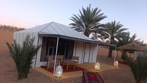 A desert tent with a covered patio, seating area, and decorative lanterns. - Nore luxury camp (Taouz)