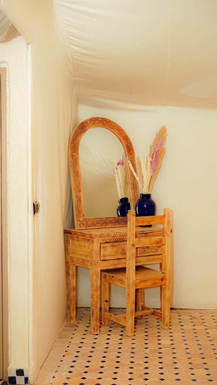 Ein Holzausziehtisch mit Spiegel und zwei Vasen mit Trockenpflanzen an einer Wand.
