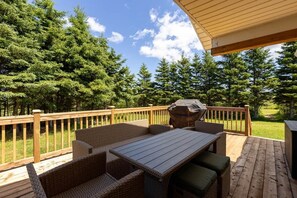 Eine Terrasse mit Tisch und Stühlen, umgeben von einem Holgitter, mit Blick auf ein bewaldetes Gebiet.
