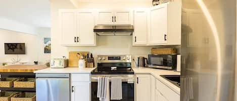 A modern kitchen with white cabinets, stainless steel appliances, and a wooden countertop.