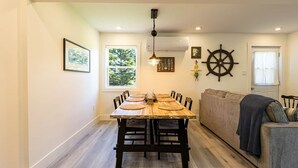 Un área de comedor con una mesa y sillas de madera, un sofá y un timón decorativo fijado a la pared.