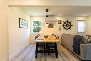 Ein Essbereich mit einem Holztisch und Stühlen, einer Couch und einer an der Wand befestigten Schiffslenken-Dekoration.
