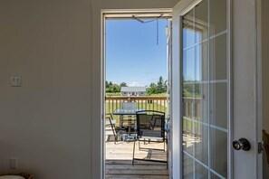 Uitzicht door een glazen deur op een patio met een tafel, stoelen, een houten terras en een huis op de achtergrond.