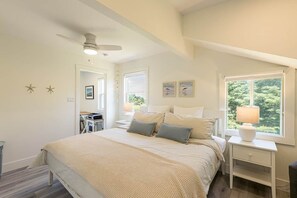 A bedroom with a bed, bedside tables, a ceiling fan, and a window with a view of greenery. - The White House - steps from Penderosa Beach (Prince Edward Island)