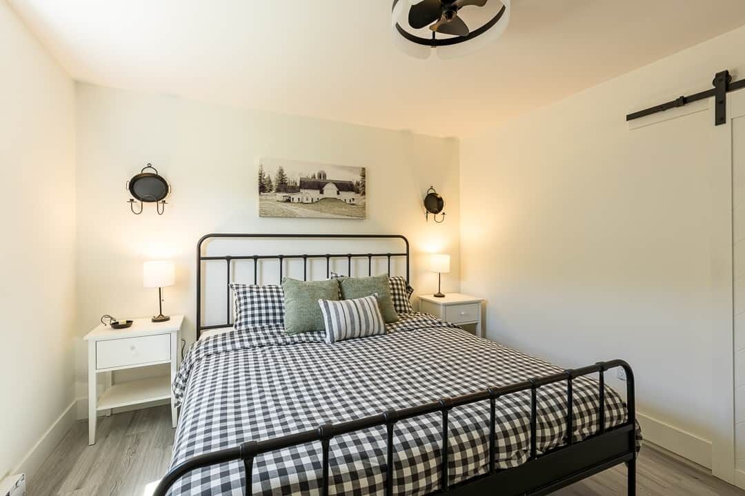 Une chambre à coucher avec une couvre-lit à carreaux, deux tables de chevet avec des lampes, un tableau accroché au mur et un ventilateur de plafond.