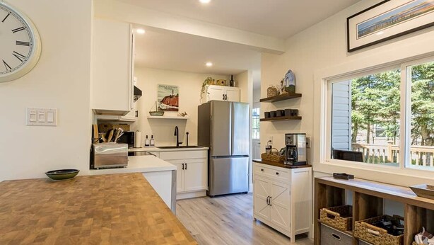 Una cocina moderna con armarios blancos, un refrigerador de acero inoxidable y una mesa de comedor de madera.