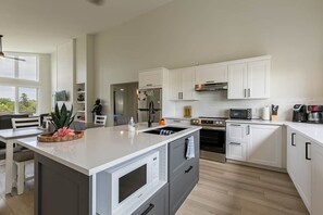 A modern kitchen with white cabinetry, a central island, and a dining area with a view. - Knights Landing in Stanley Bridge (North Rustico)