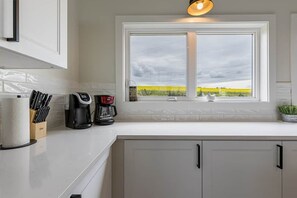 A kitchen with a window view of a field, a coffee maker, and a knife block. - Knights Landing in Stanley Bridge (North Rustico)