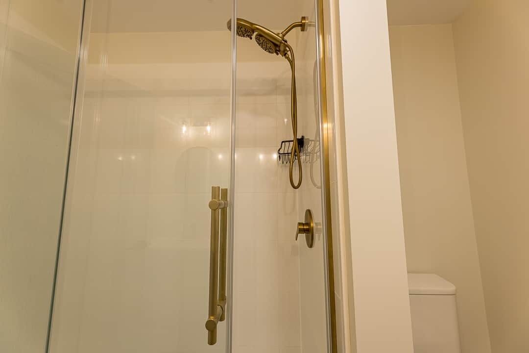 A glass-enclosed shower with a gold showerhead and control panel.