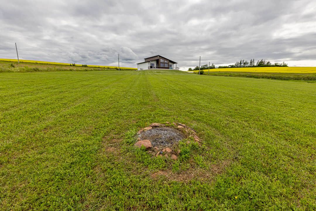 A grassy field with a circular stone structure in the foreground and a building in the background.