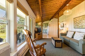 Uma sala de estar aconchegante com teto de madeira, televisão, sofá e janela com vista para um deck.