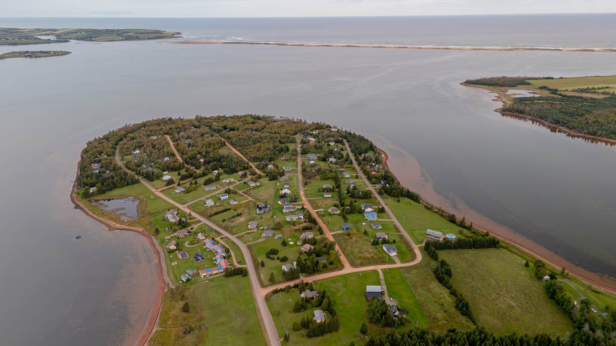 An aerial view of a coastal community with houses, roads, and a body of water.