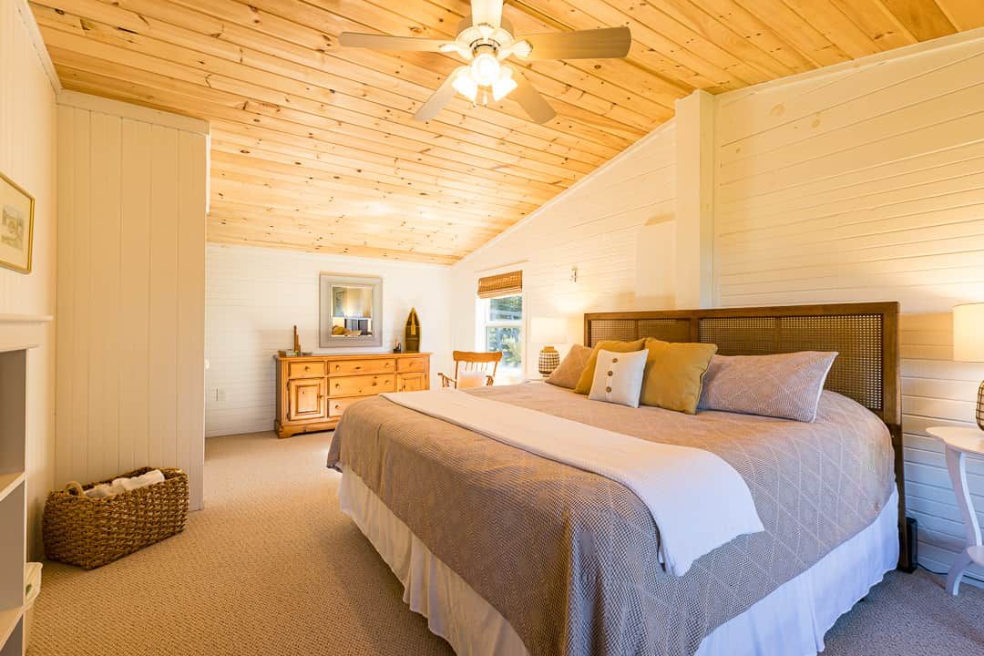 Een slaapkamer met een houten plafond, een bed met hoofdeinde, een dressoir en een spiegel.