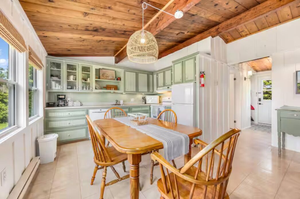 A kitchen with wooden cabinets, a dining table with chairs, and a hanging light fixture.