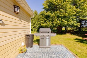A barbecue grill outside a house with a patterned rug, a trash can, and a potted plant. - Seawood Cottage on the Shore (North Rustico)