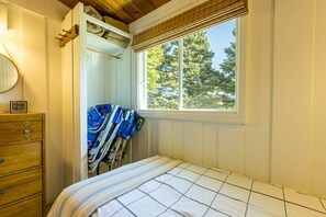 Quarto com cama, cômoda, janela com persianas e guarda-roupa com roupas penduradas.