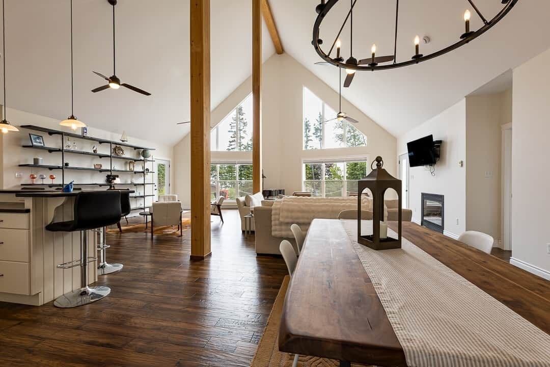 Un vaste espace de vie comprenant une longue table en bois, une cuisine avec un bar et de grandes fenêtres donnant sur l’extérieur.