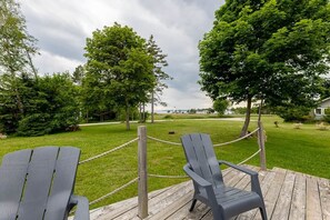 A wooden deck with two Adirondack chairs facing a grassy area with trees and a distant view of a body of water. - Lupin Lane Beach Retreat (Stratford)