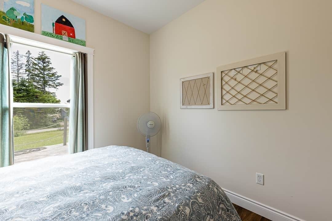 Ein Schlafzimmer mit einem Bett, einem Fenster mit Vorhängen, einem Ventilator und zwei an der Wand hängenden Bildern.
