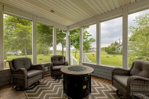 A covered porch with wicker furniture and a round table, overlooking a green landscape. - Lupin Lane Beach Retreat (Stratford)