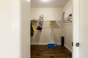A narrow hallway with a wooden floor, a white door, a fan on the wall, and a shelf with folded clothes. - Lupin Lane Beach Retreat (Stratford)