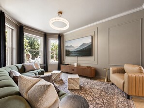 Ein modernes Wohnzimmer mit einem großen Flachbildfernseher, einer Couch, einem Couchtisch und einem gemusterten Teppich.