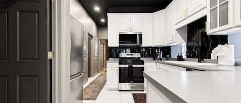 A modern kitchen with white cabinetry, stainless steel appliances, and a marble backsplash.