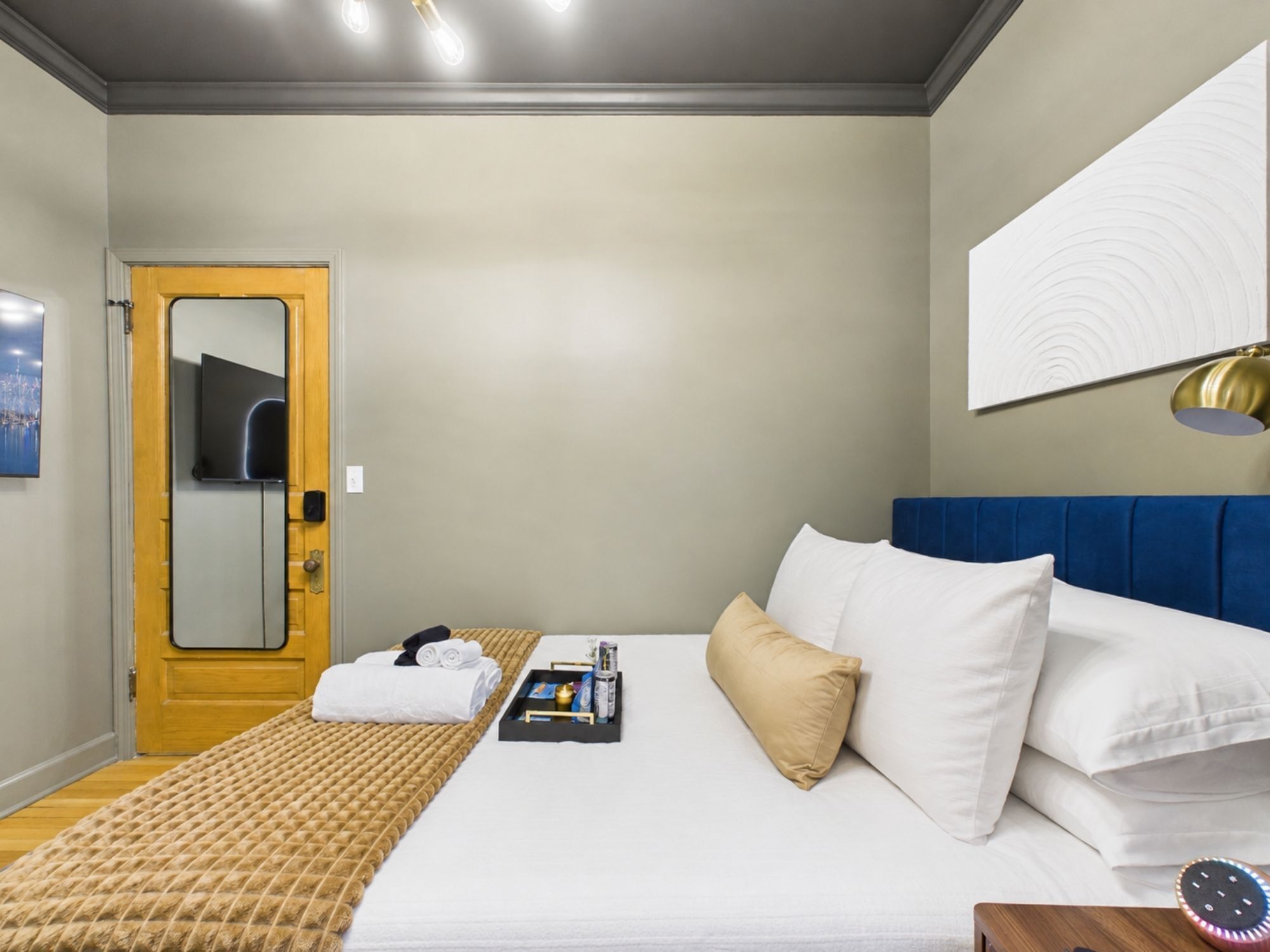 A hotel room with a bed, a bedside table, a lamp, a mirror, and a door.