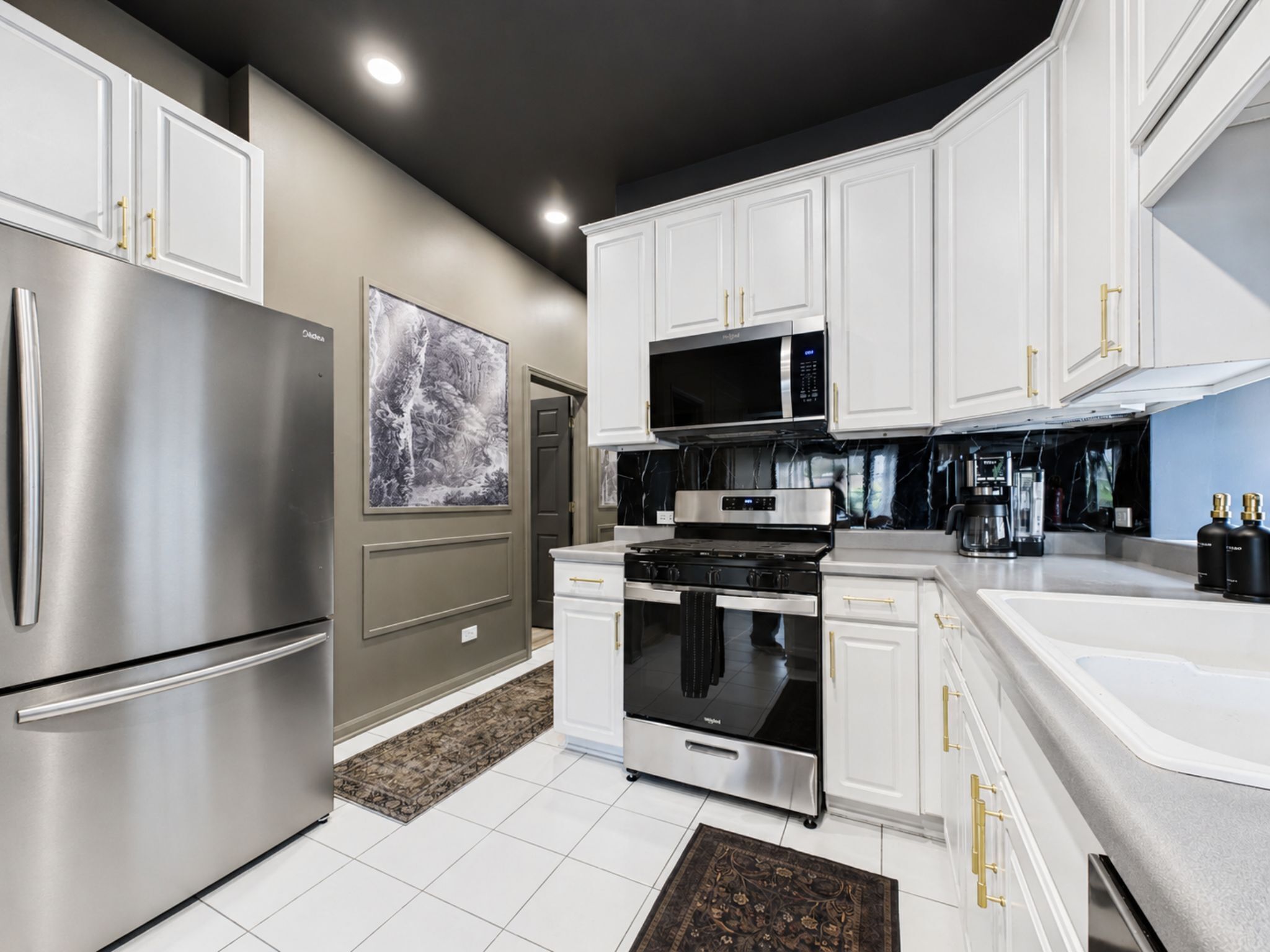 A modern kitchen with stainless steel appliances, white cabinetry, and a black and white backsplash.