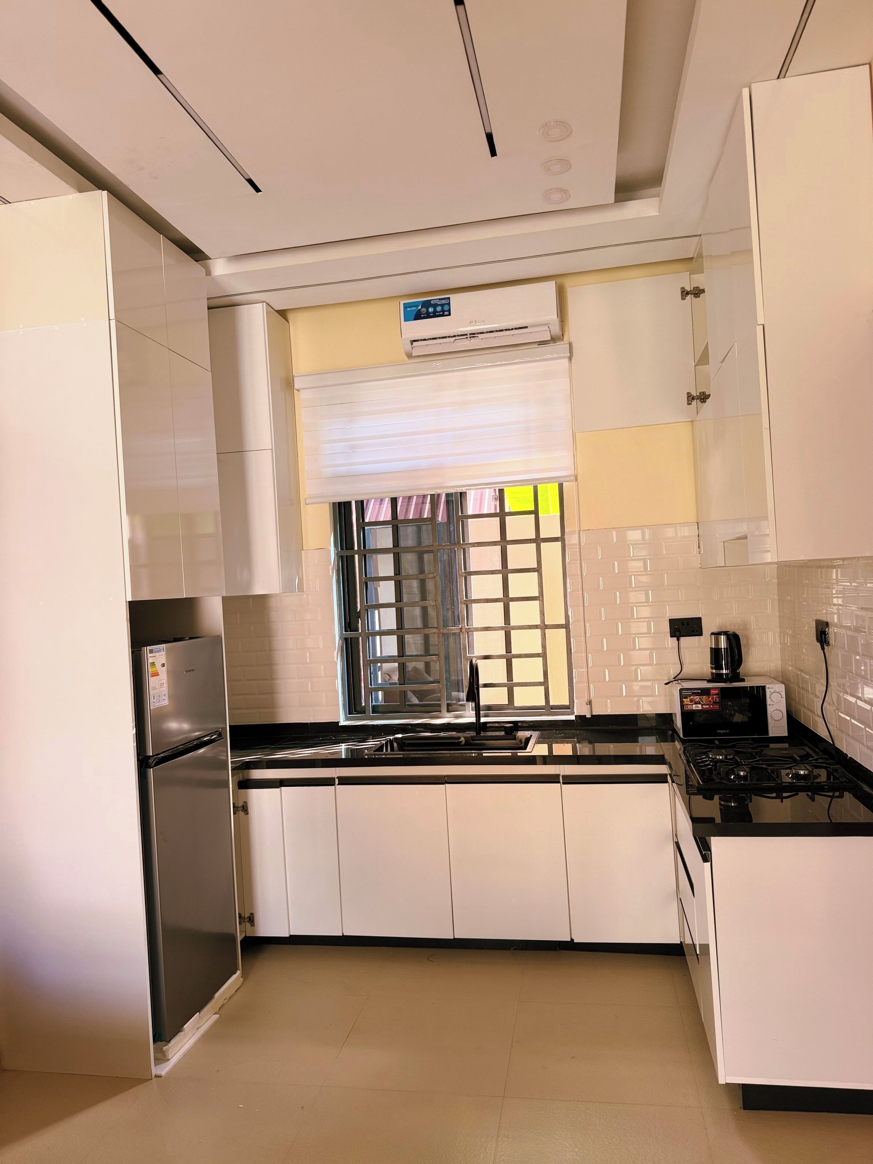 Une cuisine moderne avec des meubles blancs, un réfrigérateur en acier inoxydable, une cuisinière à gaz et un four à micro-ondes.