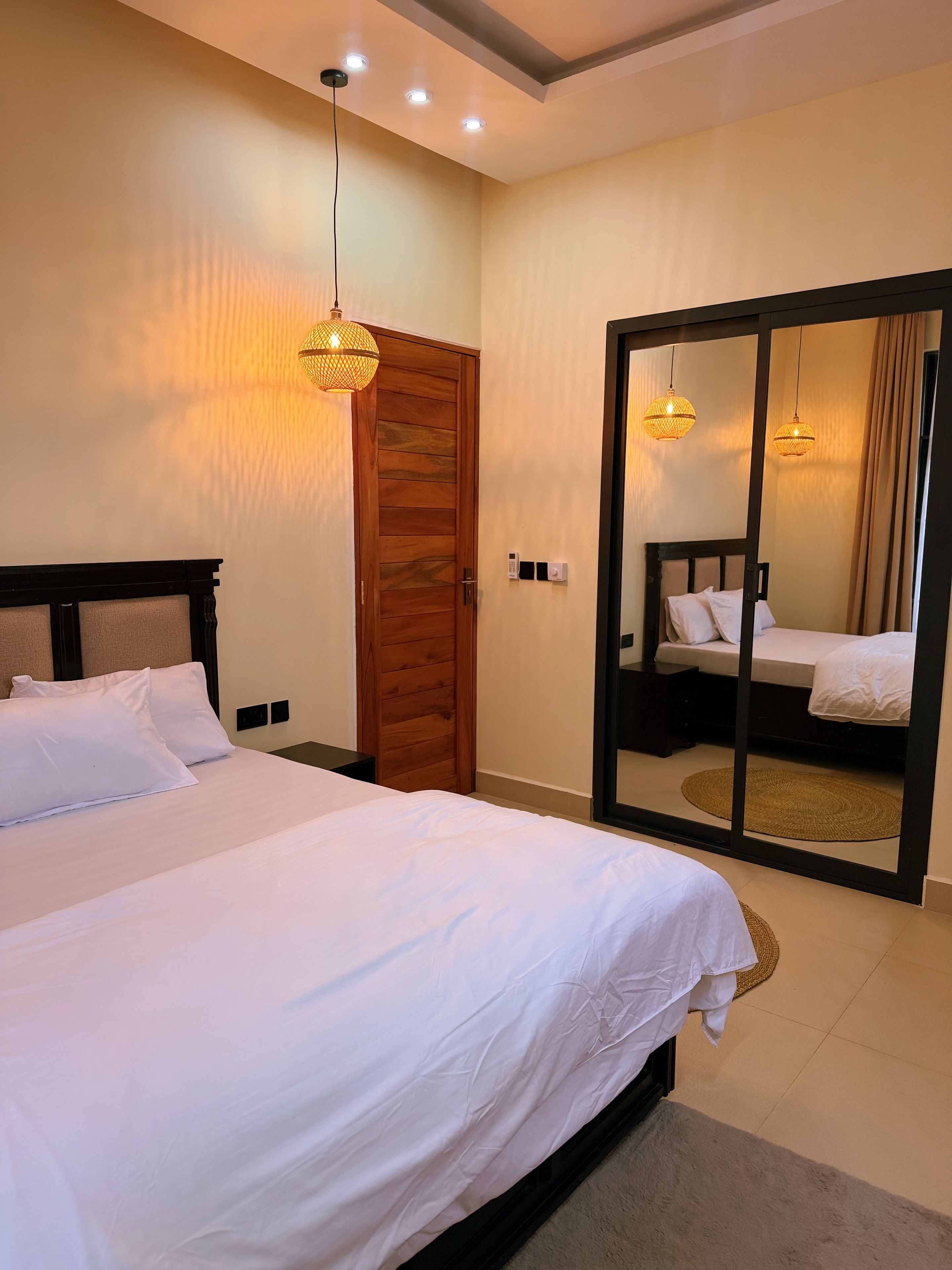 Un dormitorio con una cama grande, una puerta de madera, un espejo y una lámpara en el techo.