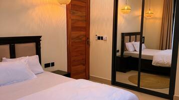 Un dormitorio con una cama grande, una puerta de madera, un espejo y una lámpara en el techo.