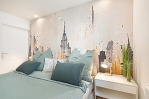 Ein Schlafzimmer mit Bett, Kissen, einem Nachttisch, einer Lampe und einer Wand mit Stadtlandschaftsmalerei.
