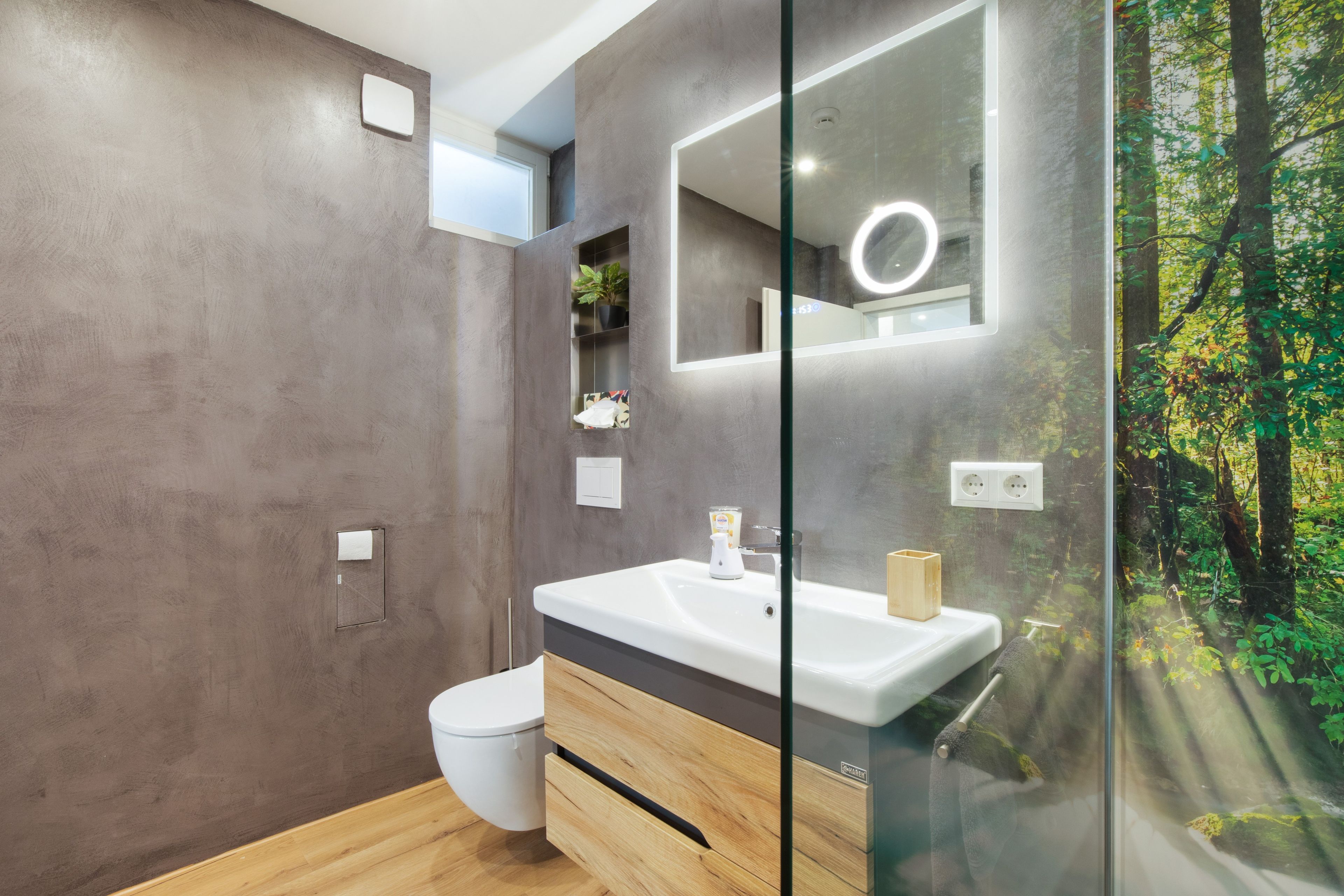 Un bany modern amb un penjador de fusta, un vas sanitari blanc, un vàter i una cabina de dutxa de vidre.