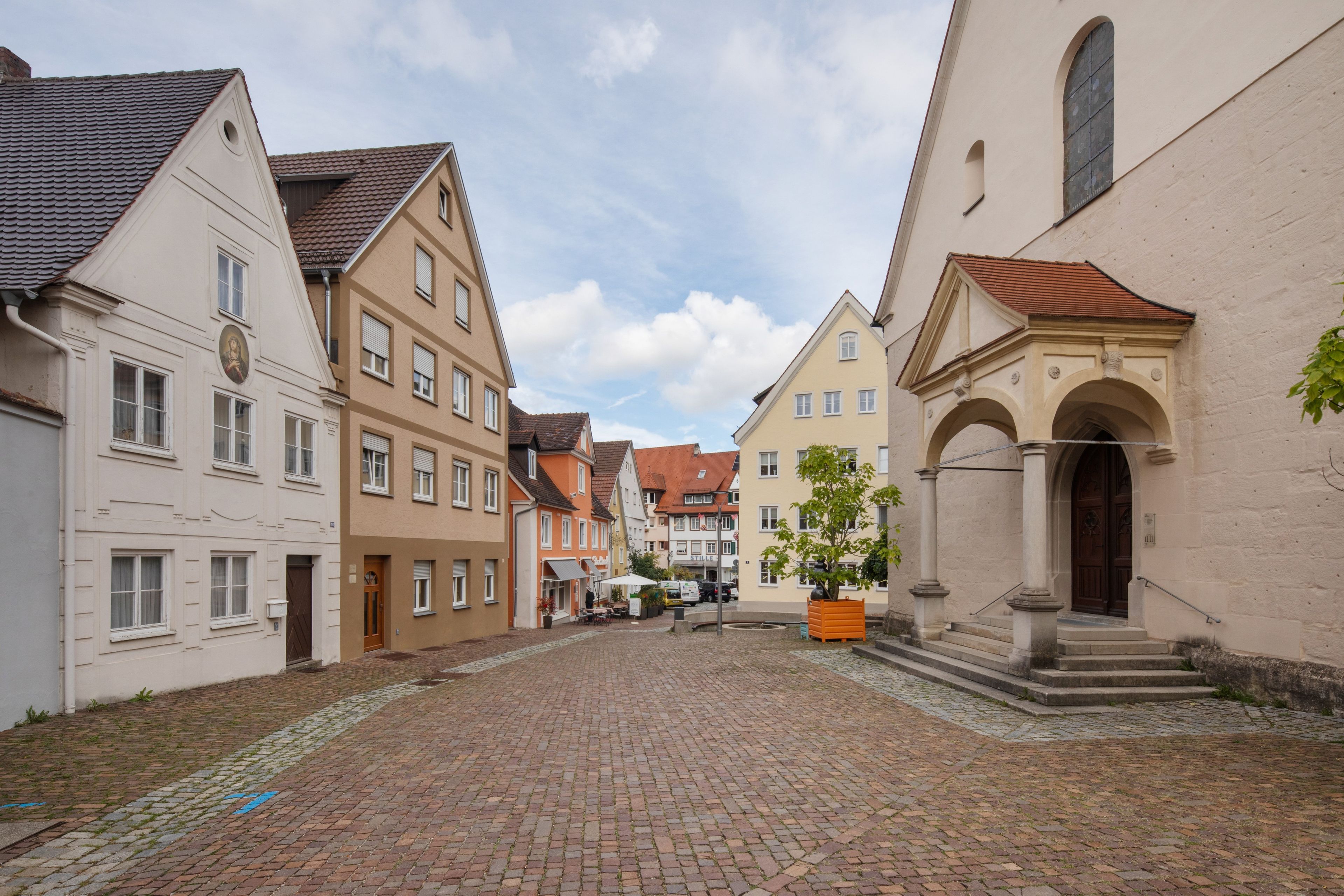 Eine Kopfsteinpflasterstraße gesäumt von traditionellen europäischen Gebäuden, darunter eine Kirche mit einem markanten Bogen.