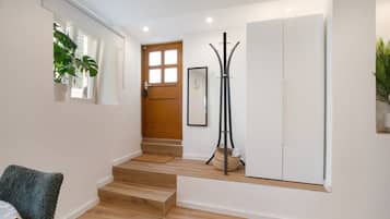 A hallway with a wooden staircase, a white door, a coat rack, and a framed picture on the wall.