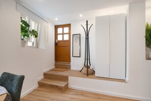 Un passadís amb una escala de fusta, una porta blanca, una perxa i un quadre al mur.