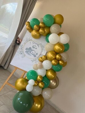 En væg med en festlig ballondekoration i grønne, hvide og guldnuancer.
