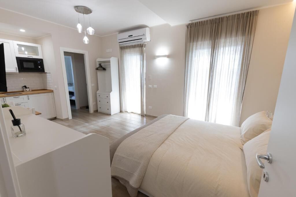 A modern hotel room with a bed, a kitchenette, a bathroom, and an air conditioning unit.