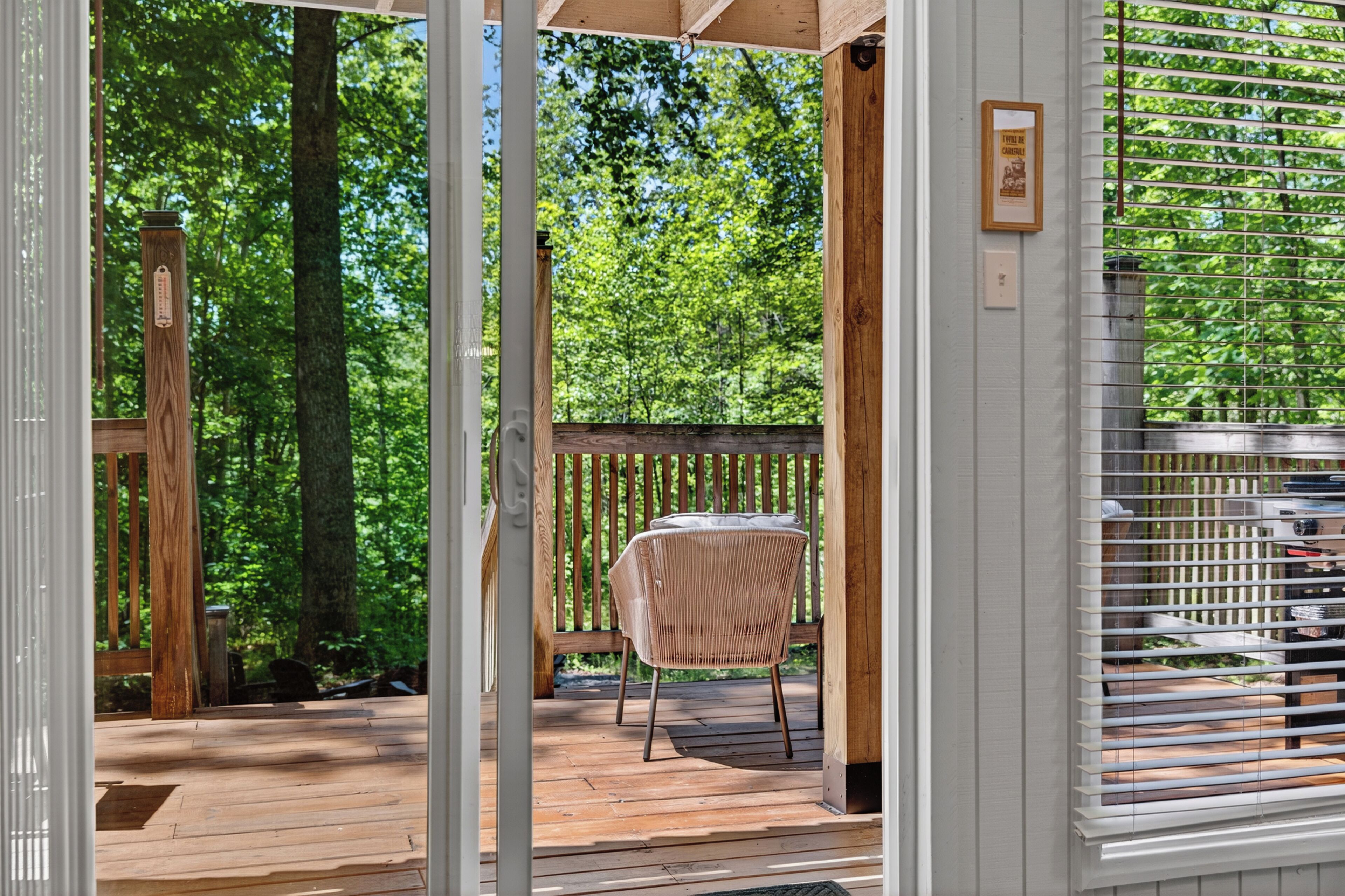 A wooden deck with a wicker chair and a table, surrounded by trees.