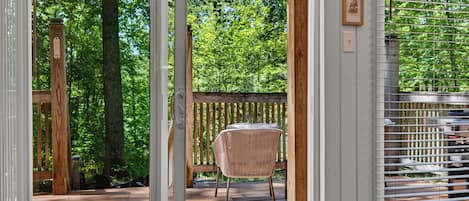 A wooden deck with a wicker chair and a table, surrounded by trees.