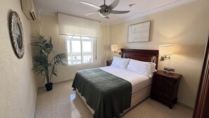 A bedroom with a bed, bedside lamps, a ceiling fan, a window with blinds, a potted plant, and a wall-mounted artwork. - Salamanca Urban (Málaga)
