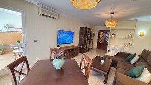 A living room with a TV, wooden furniture, a dining table, and a sofa. - Salamanca Urban (Málaga)