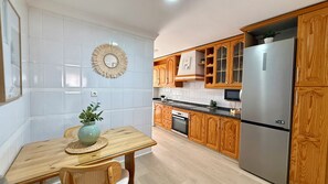 Een keuken met houten kastjes, een roestvrijstalen koelkast, een eettafel met een vaas en een spiegel aan de muur.